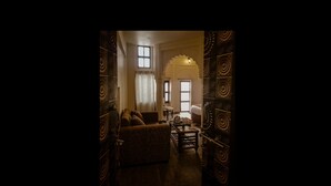 A dimly lit hallway with a sofa, a table, and a chair. There are decorative panels on the walls and a door with intricate designs. - Palace on steps (Varanasi)