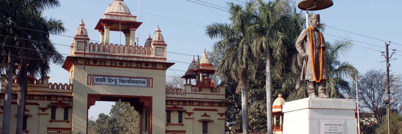 A temple entrance with a sign in a local language, a statue, and traditional architecture.