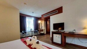 A hotel room with a bed, a desk, a television, and a seating area with chairs and a table.