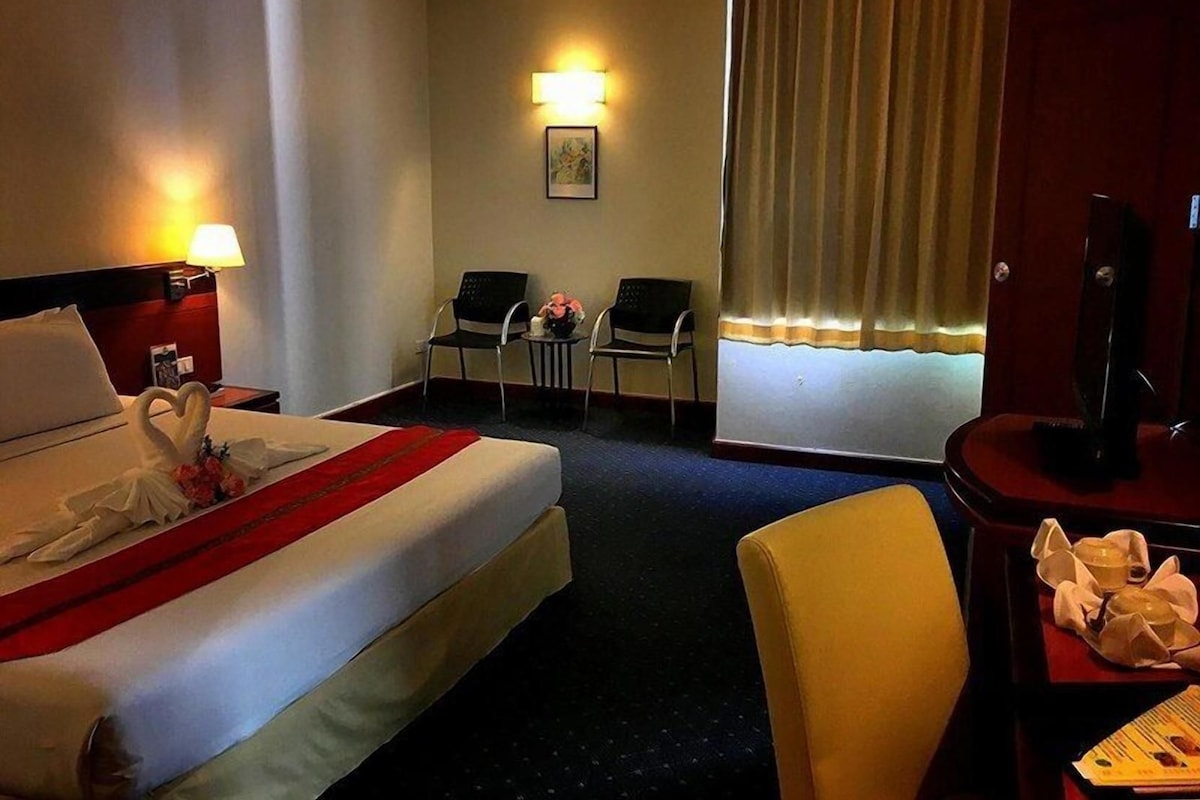 Een hotelkamer met een bed, twee stoelen, een bureau met een televisie en een raam met gordijnen.