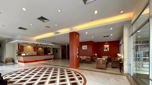 A hotel lobby with a reception desk, seating area, and a patterned floor design.
