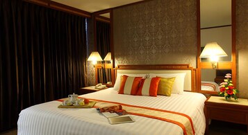 Habitación de hotel con una cama grande, dos lámparas de noche, una mesita de noche con un teléfono, un jarrón con flores y una bandeja con cosas para el desayuno.