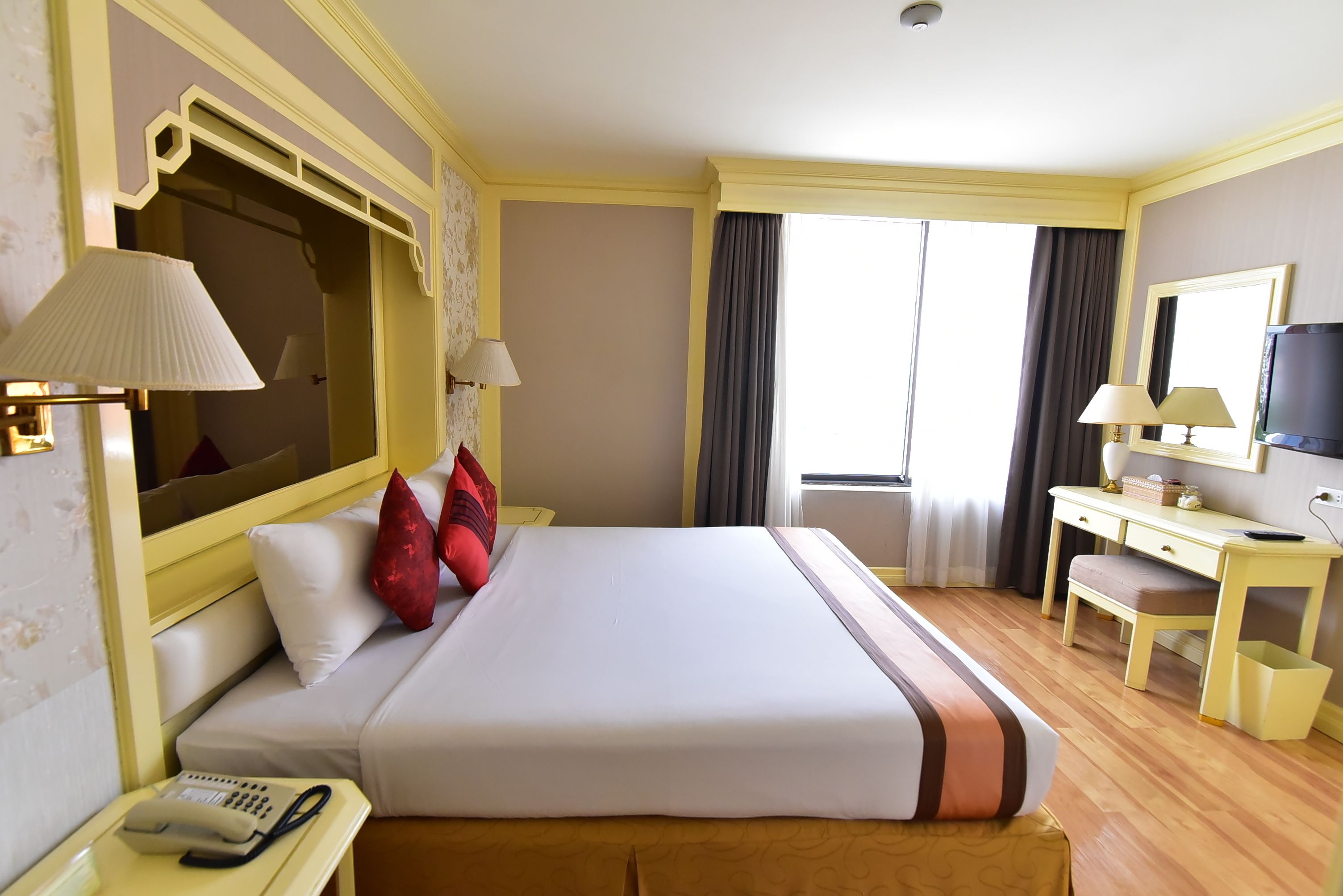 A hotel room with a bed, bedside lamps, a desk with a chair, a television, and a large mirror.