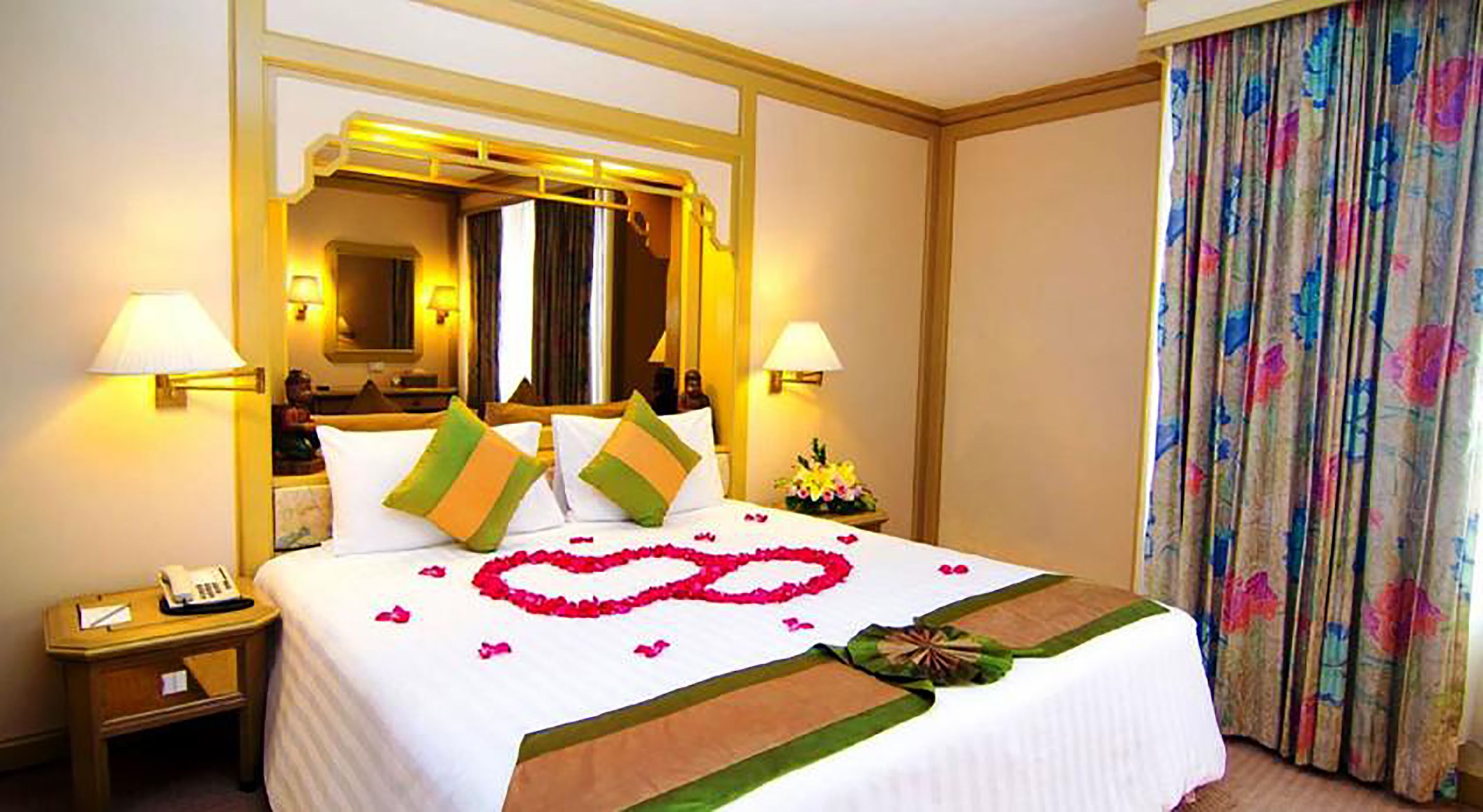 A hotel room with a large bed, two bedside lamps, a nightstand with a phone, and a floral curtain.