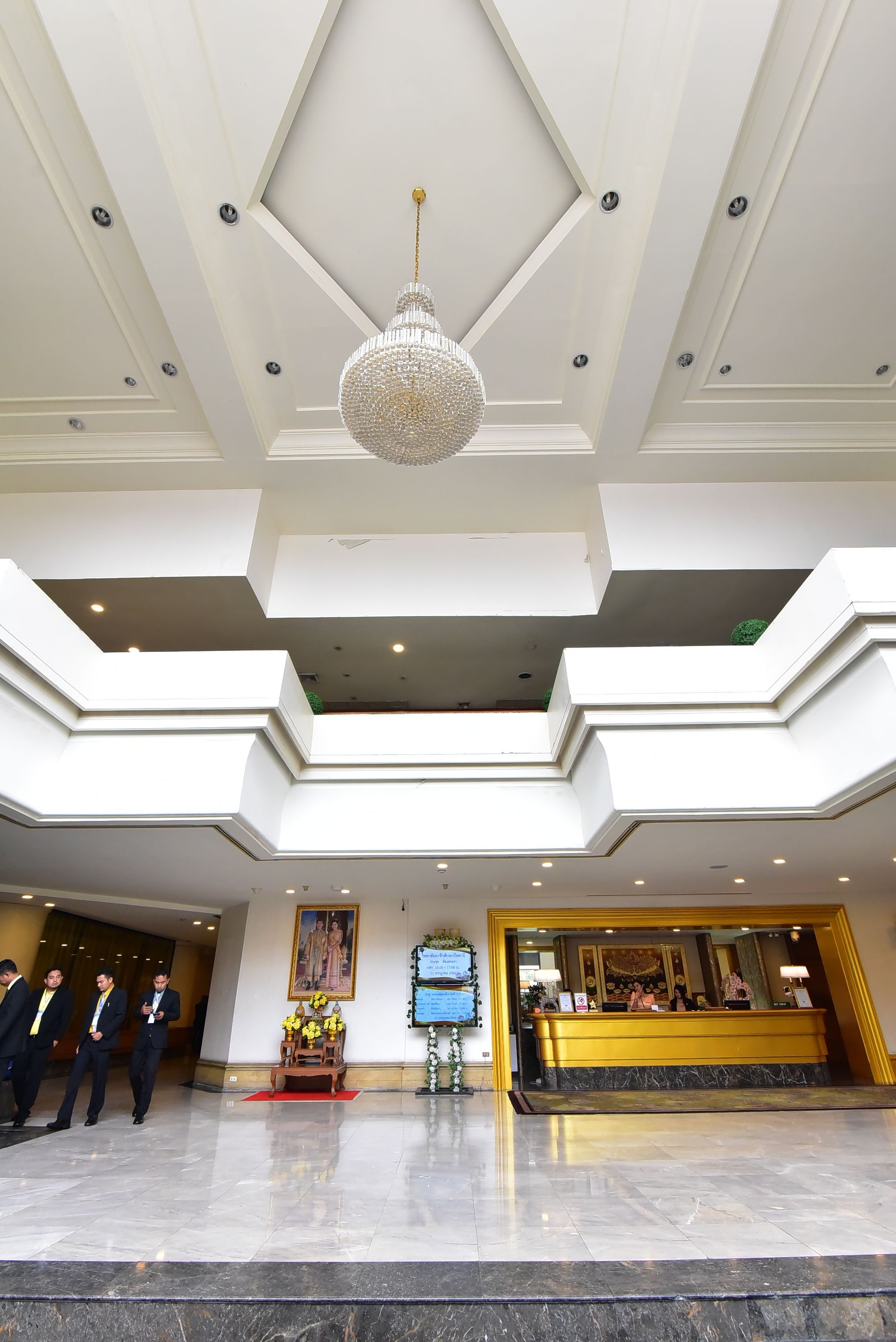 A hotel lobby with a high ceiling, a chandelier, a reception desk, and a red carpet.