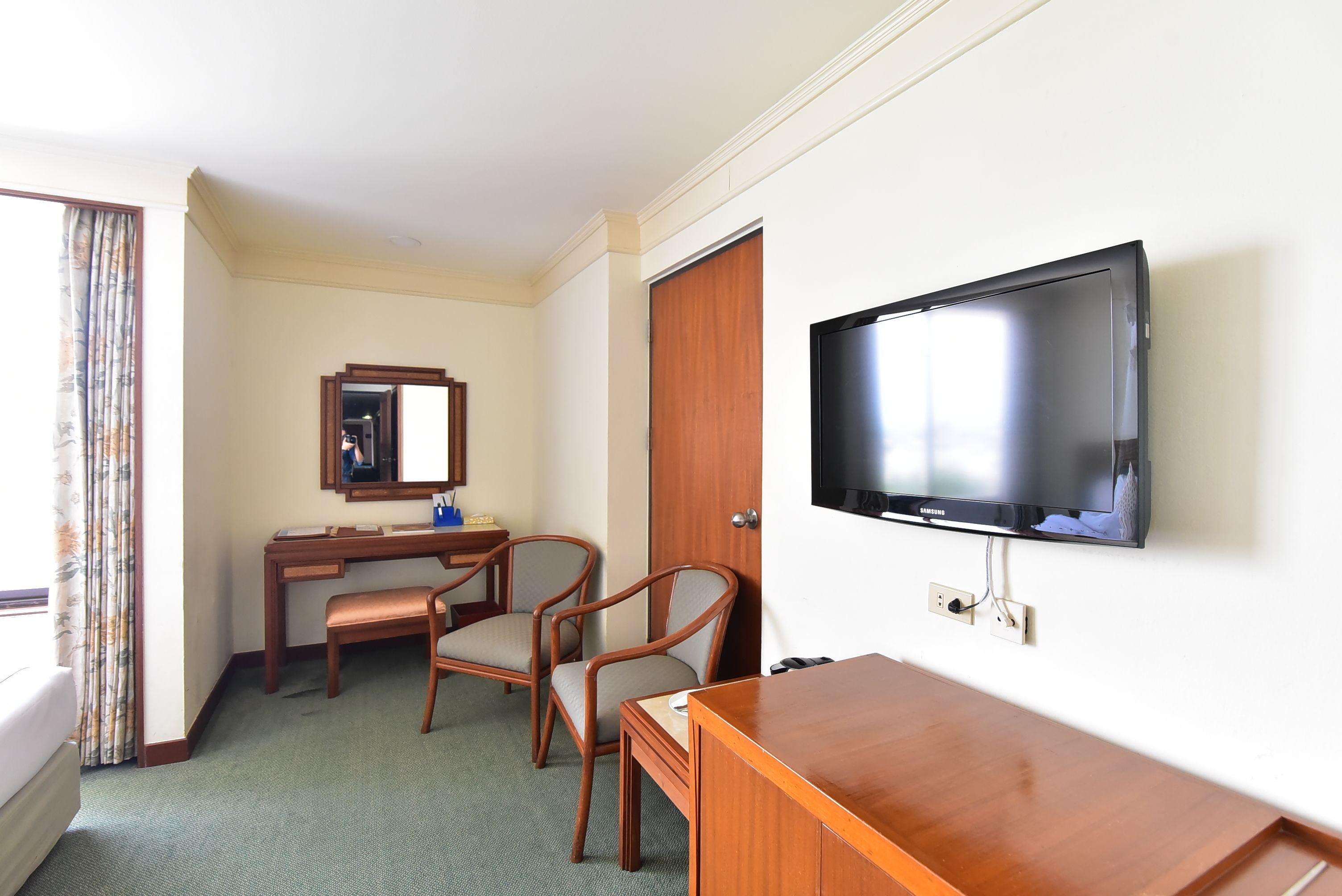 A hotel room with a bed, a desk, two chairs, a television, and a wardrobe.