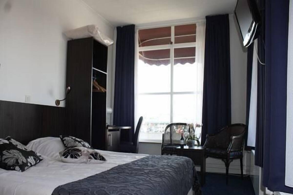 A hotel room with a bed, a chair, a desk, and a window with curtains.