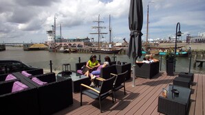 En terrass med utomhusmöbler och utsikt över en hamn med båtar.