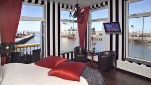 Ett hotellrum med en stor säng, en TV och utsikt över en hamn.