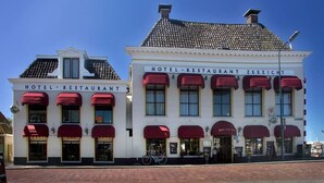 Ett hotell med en klassisk fasad, med en skylt som visar texten ”HOTEL RESTAURANT ZEEZICHT” och en cykel parkerad framför.
