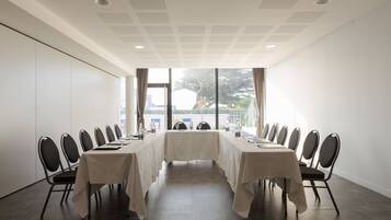 A conference room with a long table and chairs, large windows, and a white ceiling.
