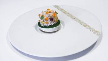 Een wit bord met een klein, rond, wit dessert op een groene ondergrond, versierd met goudvlokken en kleurrijke details.