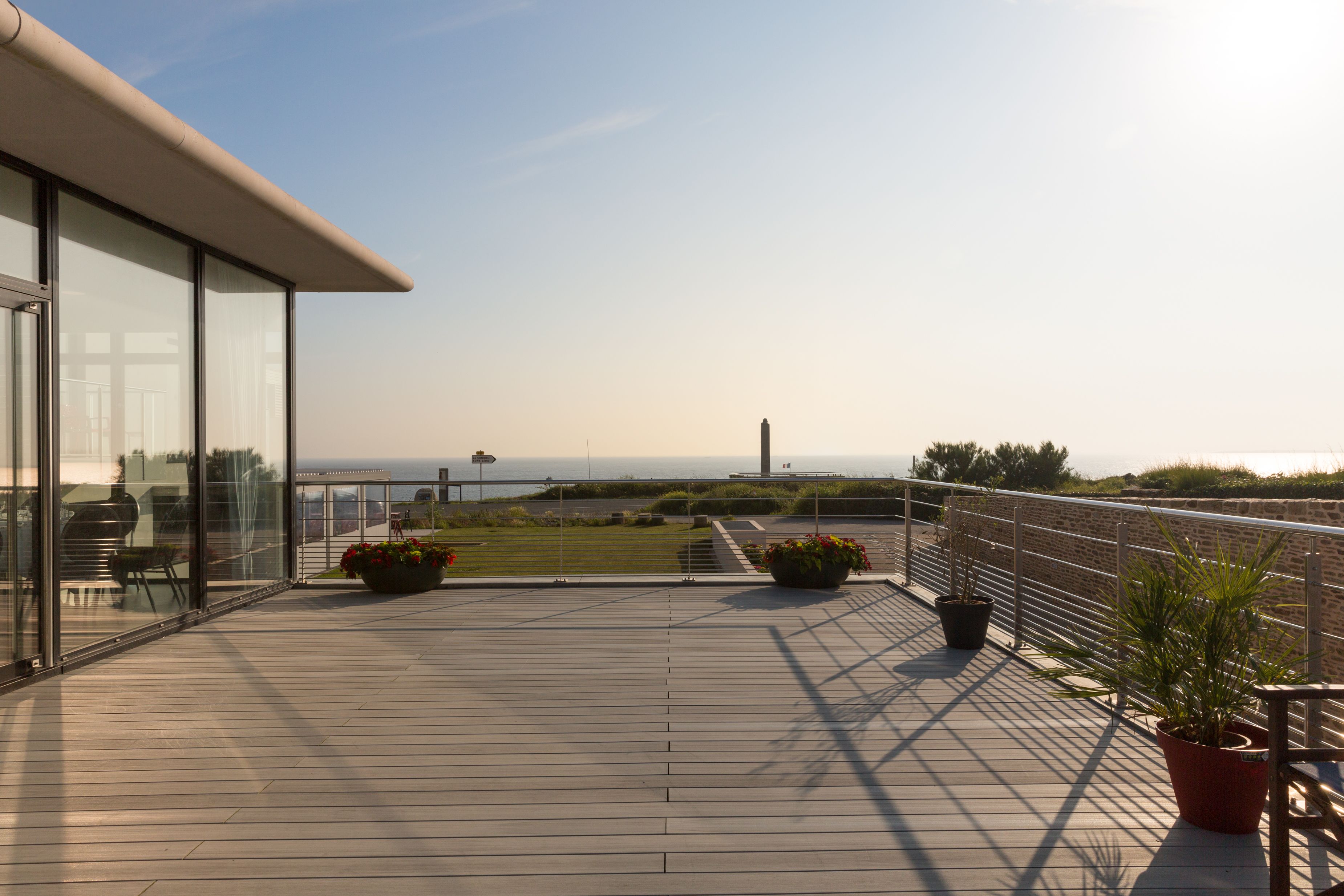 A deck with potted plants, a railing, and a view of the sea.