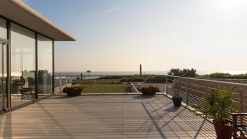 A deck with potted plants, a railing, and a view of the sea.