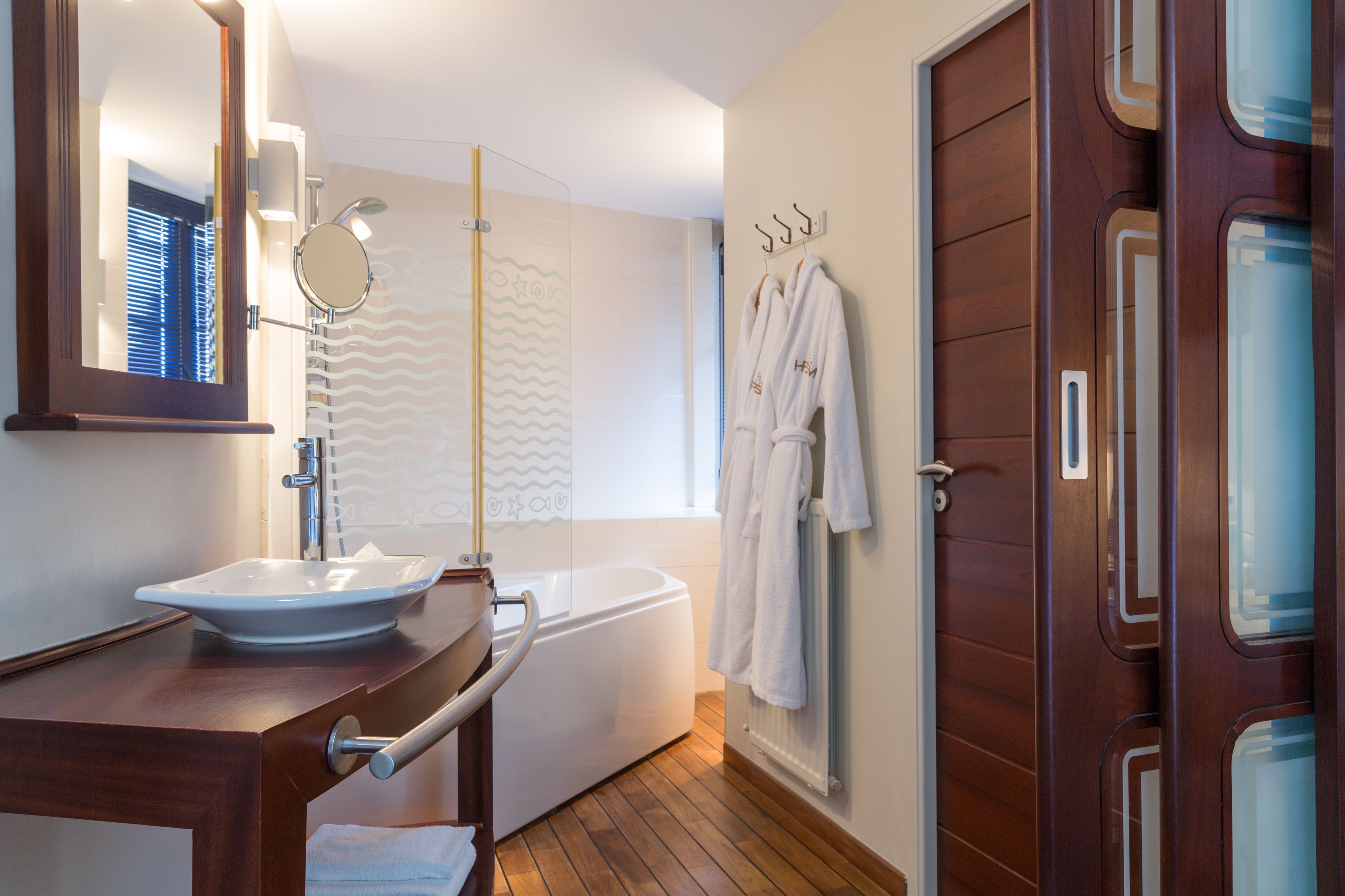 A modern bathroom with a wooden vanity, a white sink, a bathtub, and a glass shower enclosure.