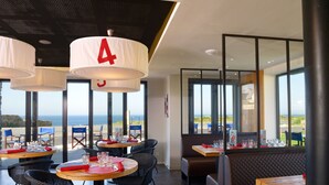 Un restaurante con mesas redondas, sillas de mimbre y amplias ventanas que dan al mar.