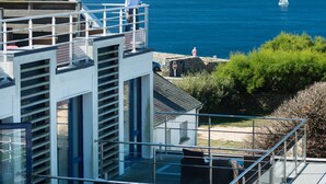Un edificio moderno con balcón que da al mar, con mobiliario exterior y una vista despejada del océano.