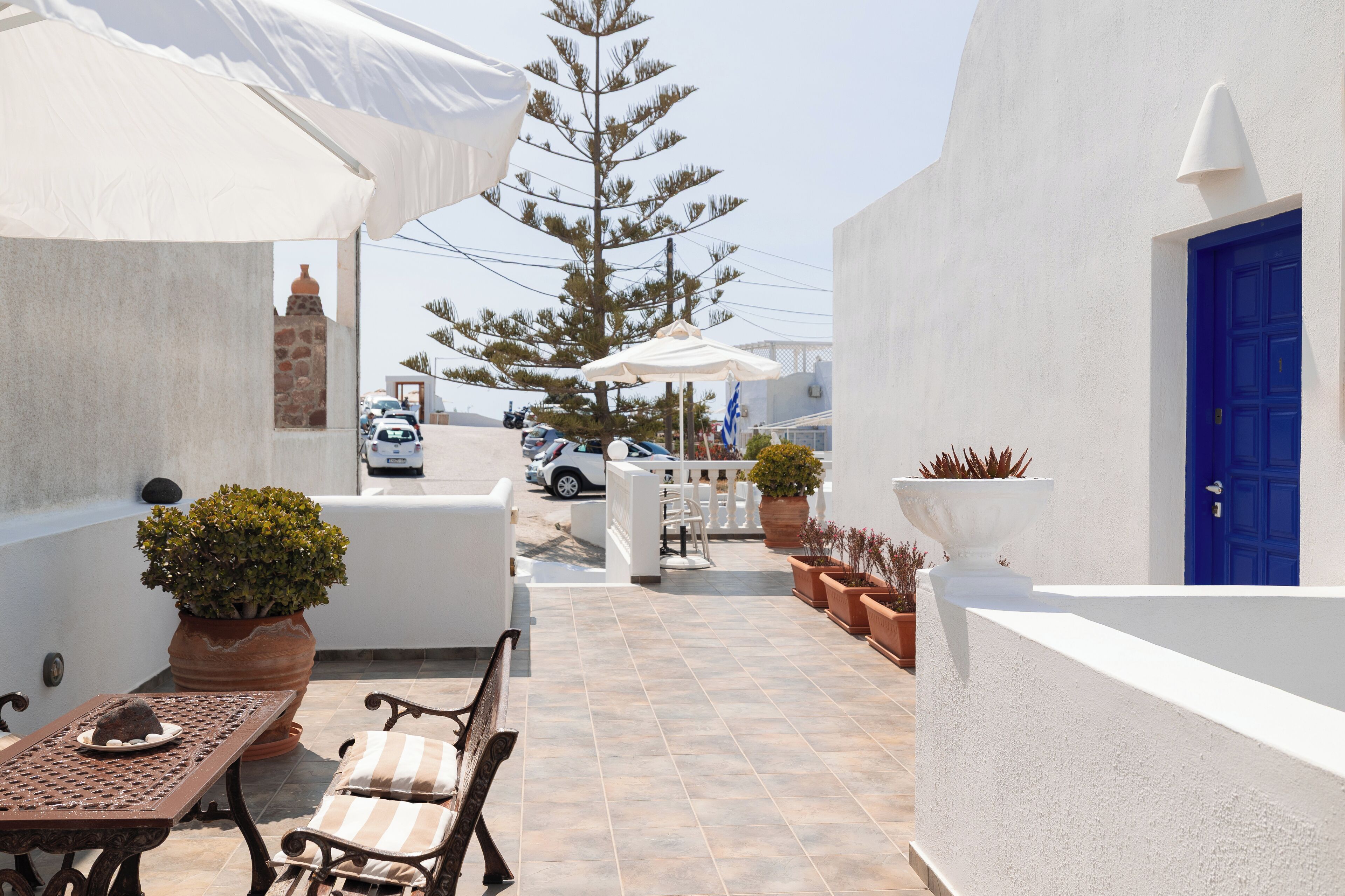A terrace with outdoor seating, potted plants, and a view of the street.