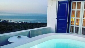 A balcony with a view of the sea and buildings, a blue door, and a bathtub. - Villa Happening (Santorini)