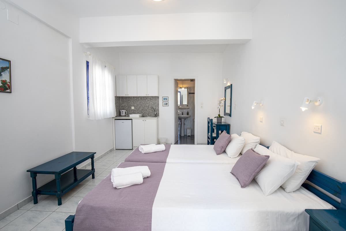 A hotel room with a bed, a bench, a small kitchen area, and a bathroom visible through an open door.
