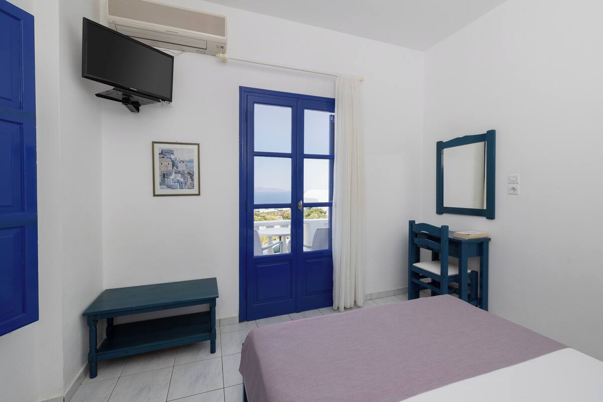 A bedroom with a bed, a TV, a desk, a chair, and a window with a view.