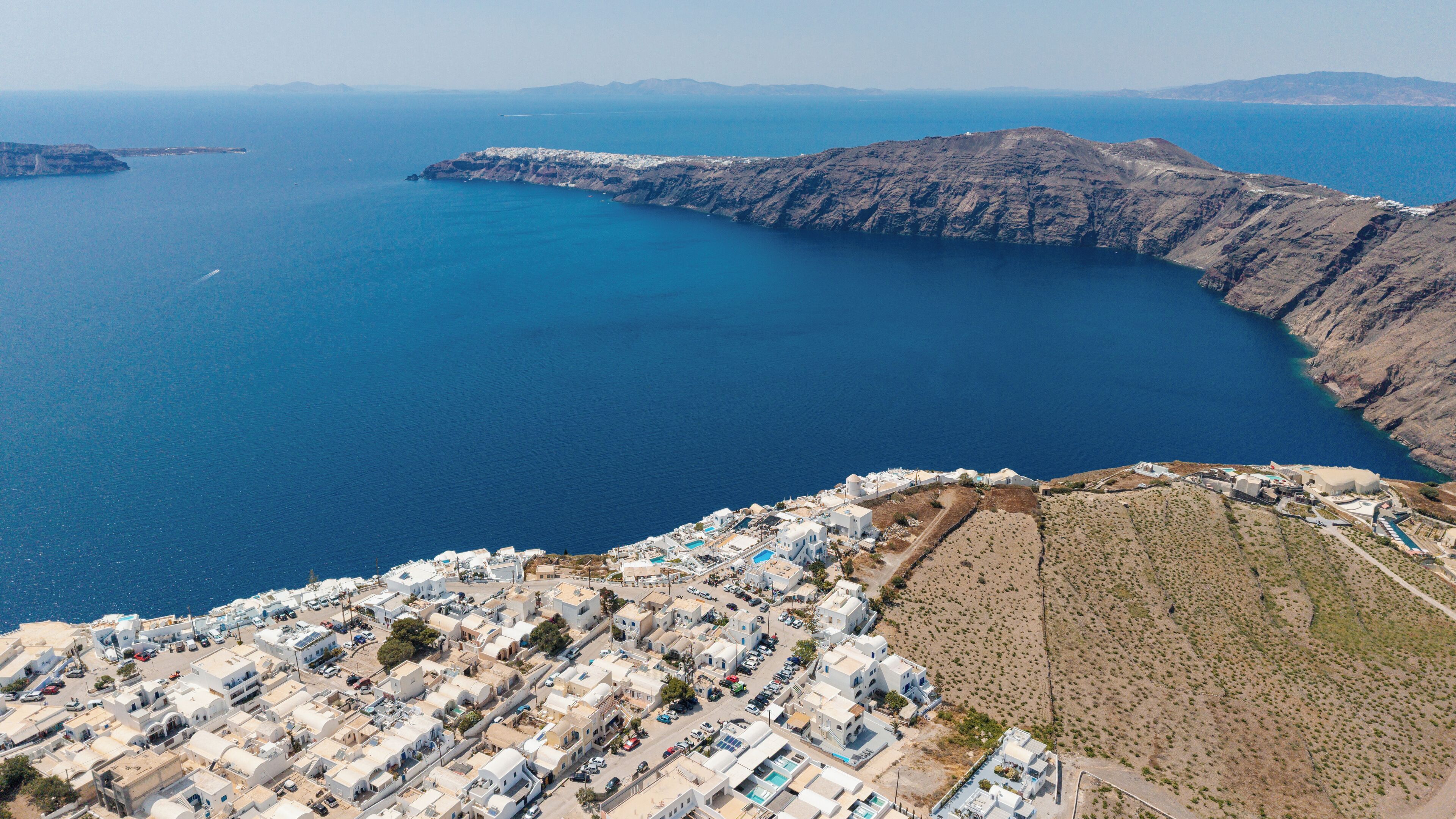 Vista aérea de un pueblo costero con edificios blancos, un mar azul cristalino y un litoral escarpado.