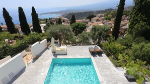 Una piscina en la azotea con vistas a un pueblo costero, rodeada de árboles y un cielo despejado.