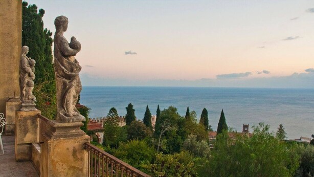 Un balcón con estatuas de piedra con vistas a un pueblo costero.