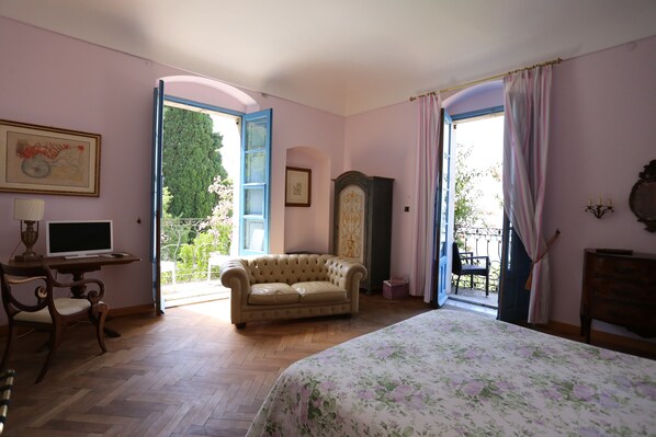 A bedroom with a bed, a desk, a chair, a sofa, and a wardrobe. There are two doors leading to an outdoor area.