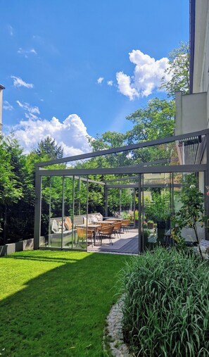 A modern outdoor patio with glass walls, a lawn, and a stone pathway.
