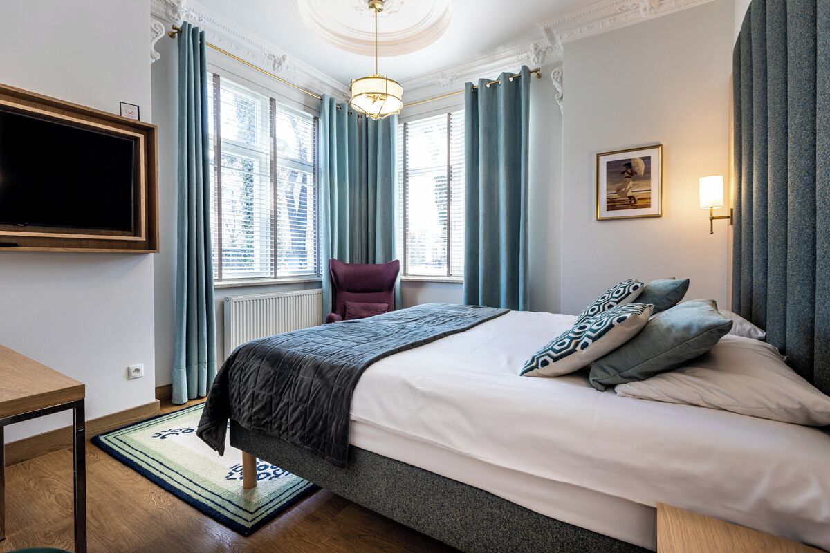 A bedroom with a bed, a chair, a TV, and a window with curtains.