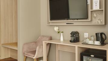 A modern room with a wooden floor, a pink chair, a desk with a TV, a coffee machine, and a mini-fridge.
