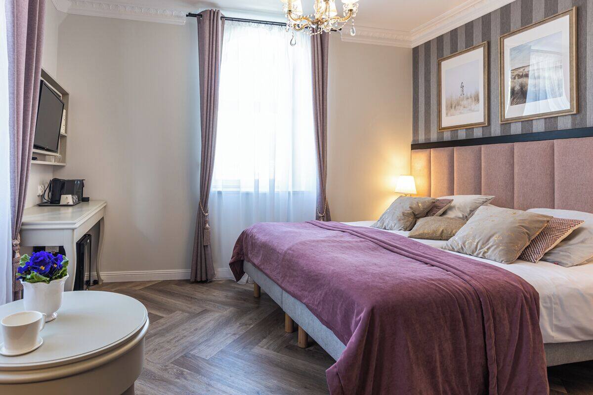 A hotel room with a bed, a bedside table, a TV, and a window with curtains.
