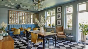 A dining area with a checkered floor, a wooden table, and chairs. There is a large window with a view of greenery outside. - Villa Antonina (Sopot)
