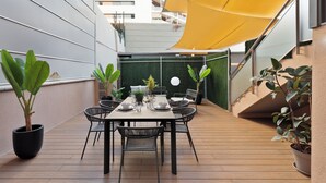Une terrasse sur le toit, avec une table à manger pour quatre personnes, entourée de plantes en pot et d’un auvent jaune.