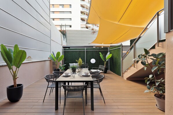 A rooftop terrace with a dining table set for four, surrounded by potted plants and a yellow canopy. - Apartments Sata Olimpic Village Area (Barcelona)
