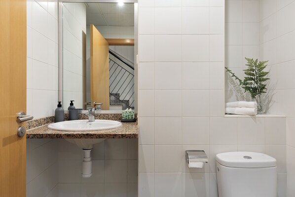 A bathroom with a granite countertop sink, a mirror, a toilet, and a small shelf with a plant. - Apartments Sata Olimpic Village Area (Barcelona)
