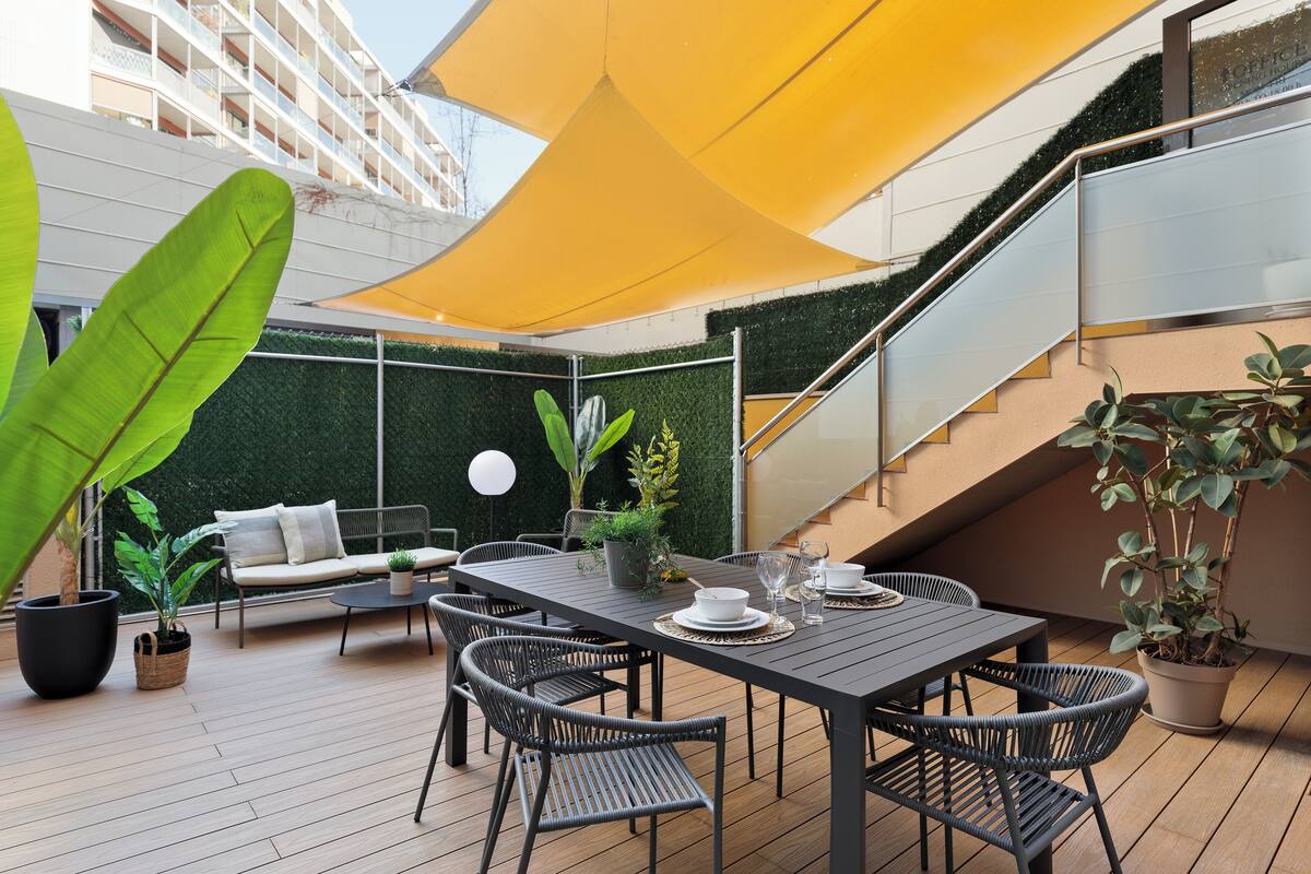Eine Terrasse im Freien mit Esstisch, Stühlen und einem gelben Sonnensegel.
