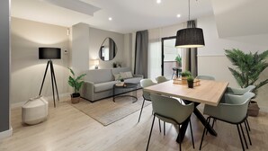 Un salon moderne avec un canapé, une table basse et une table à manger avec des chaises. On y trouve une lampe, un miroir et une plante en pot.