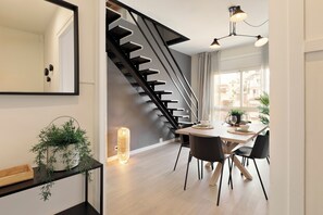 Un espace repas moderne comprenant un escalier, une table à manger avec des chaises et un luminaire suspendu.