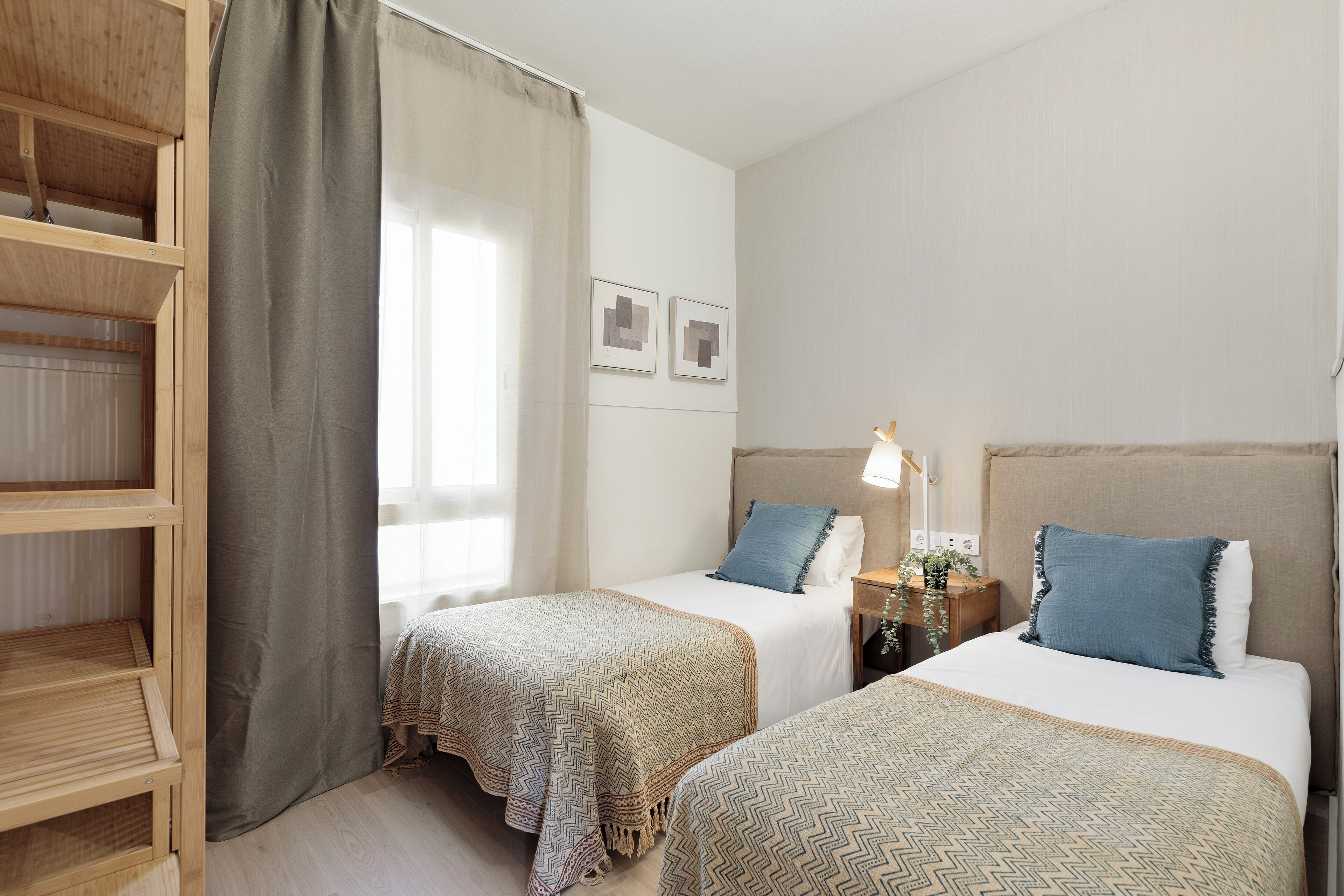 Een hotelkamer met twee bedden, een houten kastje, een nachtkastje met lamp en een raam met gordijnen.