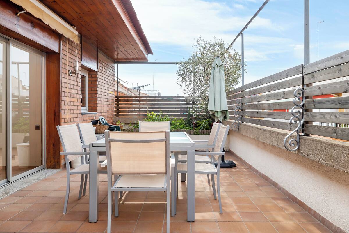 Een terras buiten met een tafel en stoelen, een houten omheining en uitzicht op de omgeving.