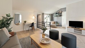 Un salon moderne comprenant un canapé, un pouf, une table basse et un téléviseur posé sur un meuble en bois.