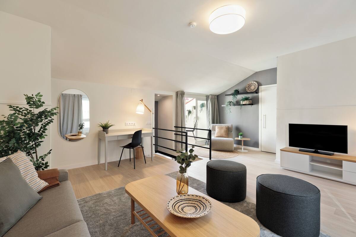 Een moderne woonkamer met een bank, een voetenbankje, een salontafel en een televisie op een houten dressoir.
