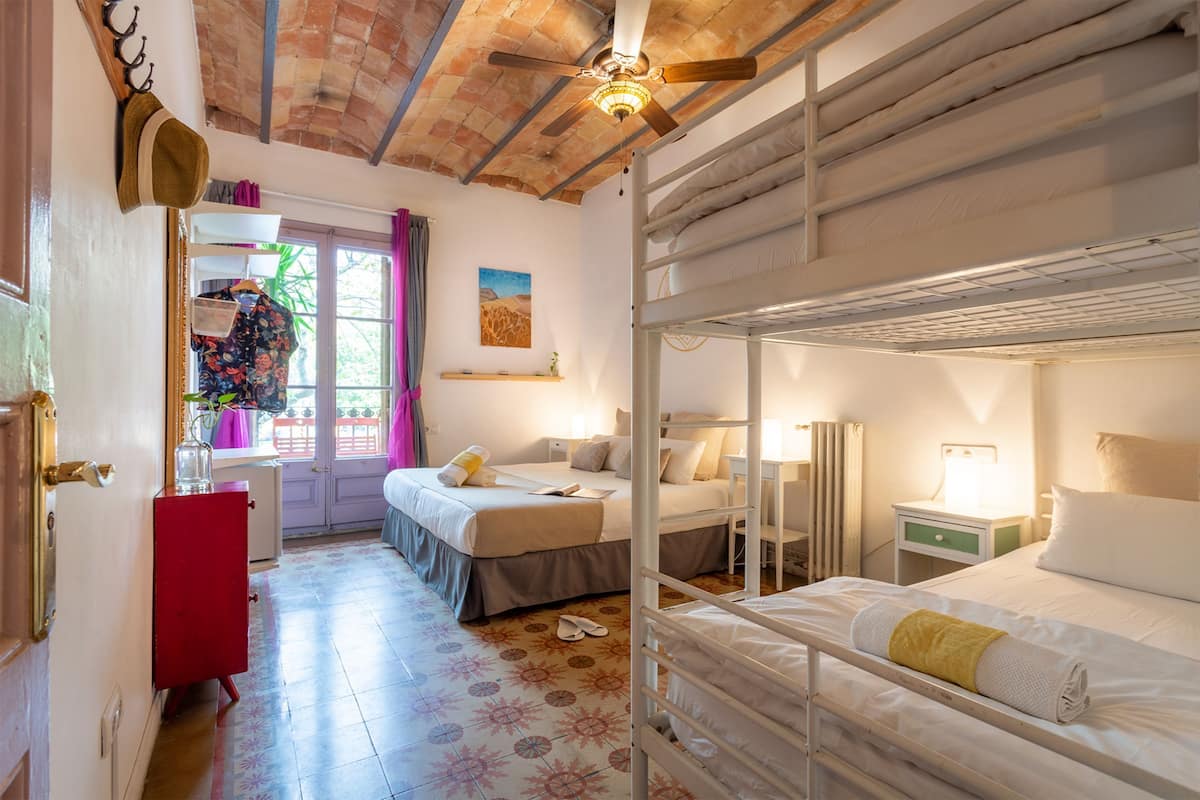 Ein Zimmer mit zwei Betten, einem roten Schrank, einem Fenster mit Vorhängen und einem Deckenventilator.