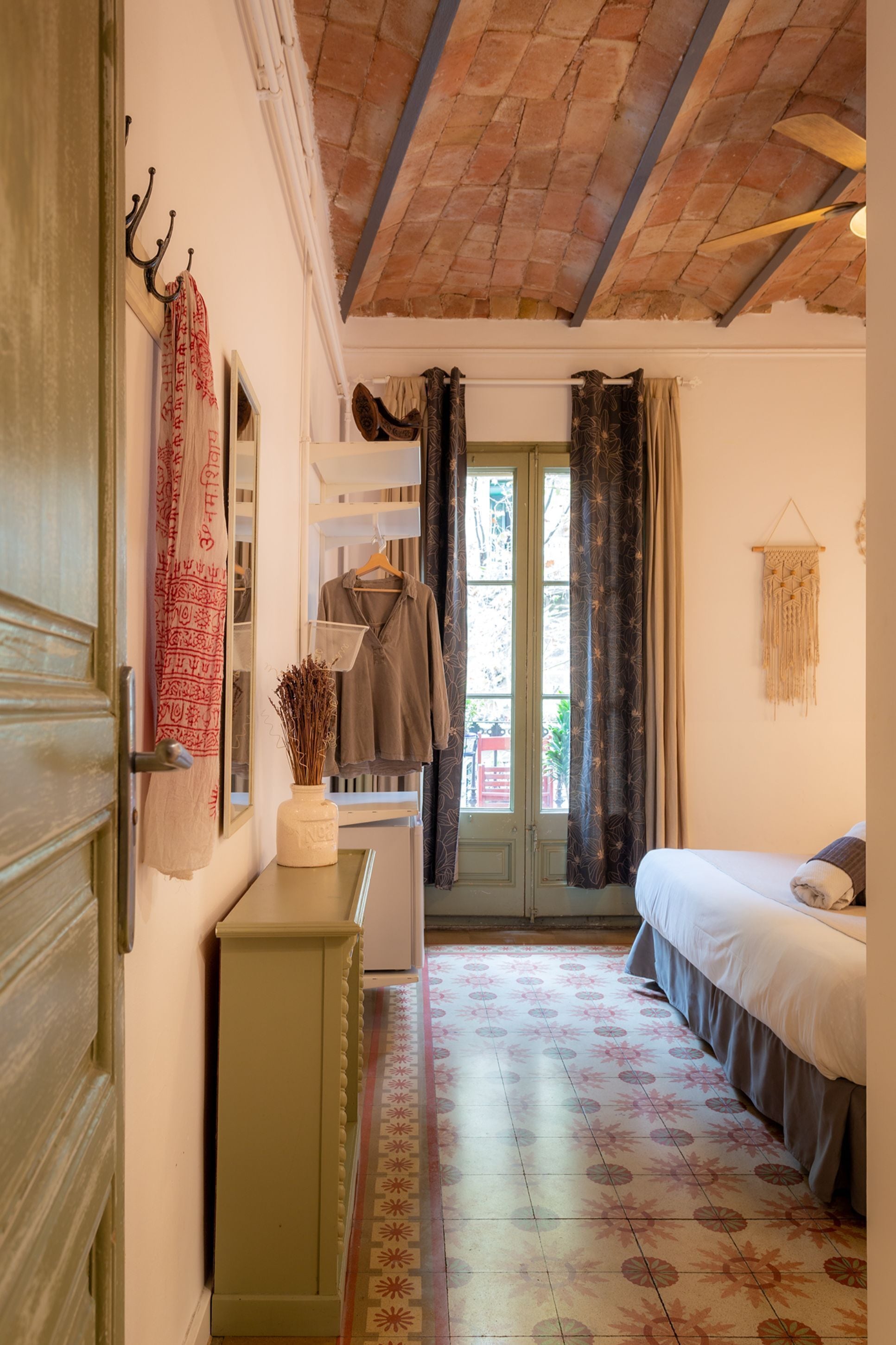 A room with a bed, a dresser, a mirror, a hanging coat rack, and a window with curtains.