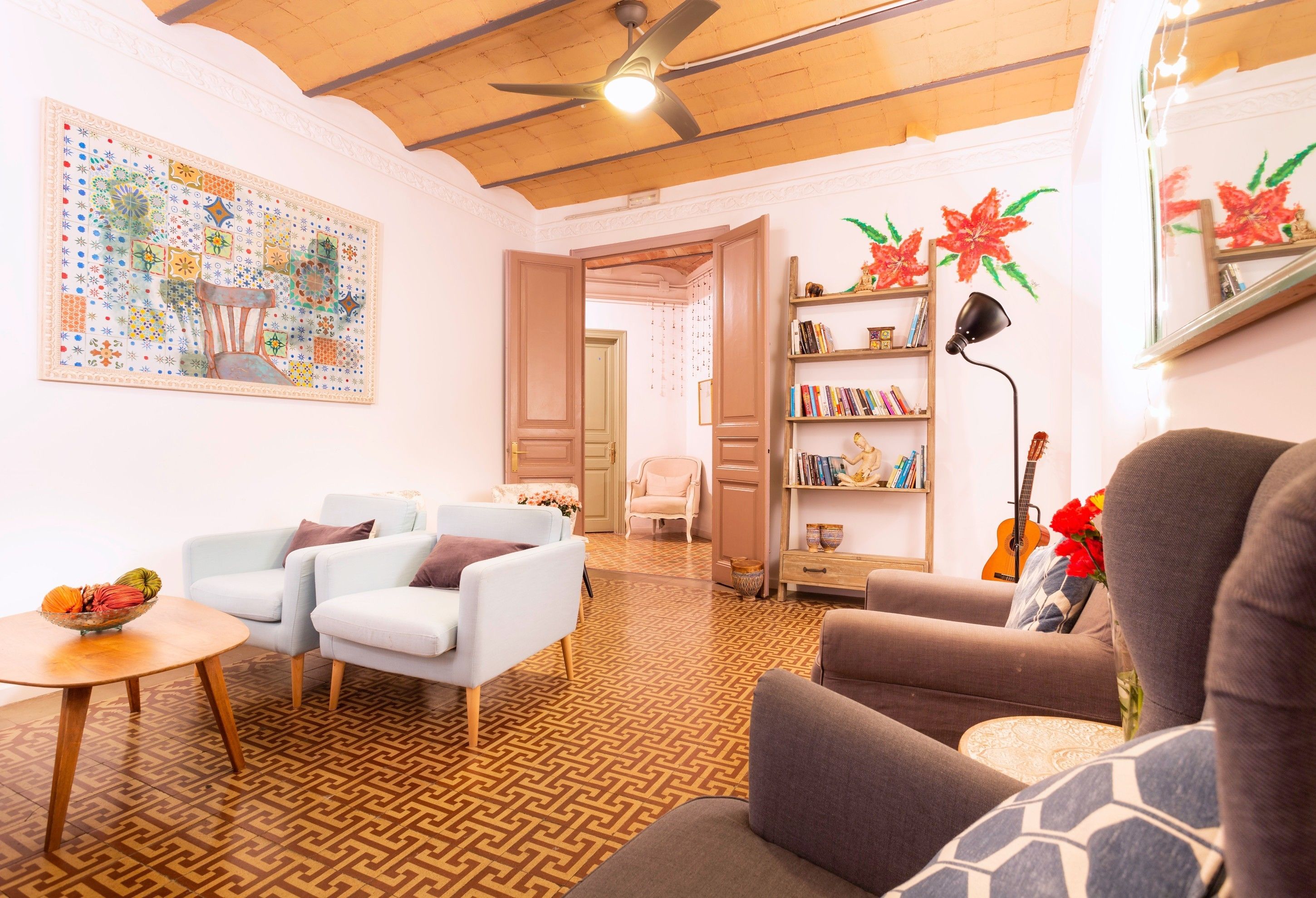 A living room with a patterned floor, a ceiling fan, a bookshelf, and a dining area with a table and chairs.
