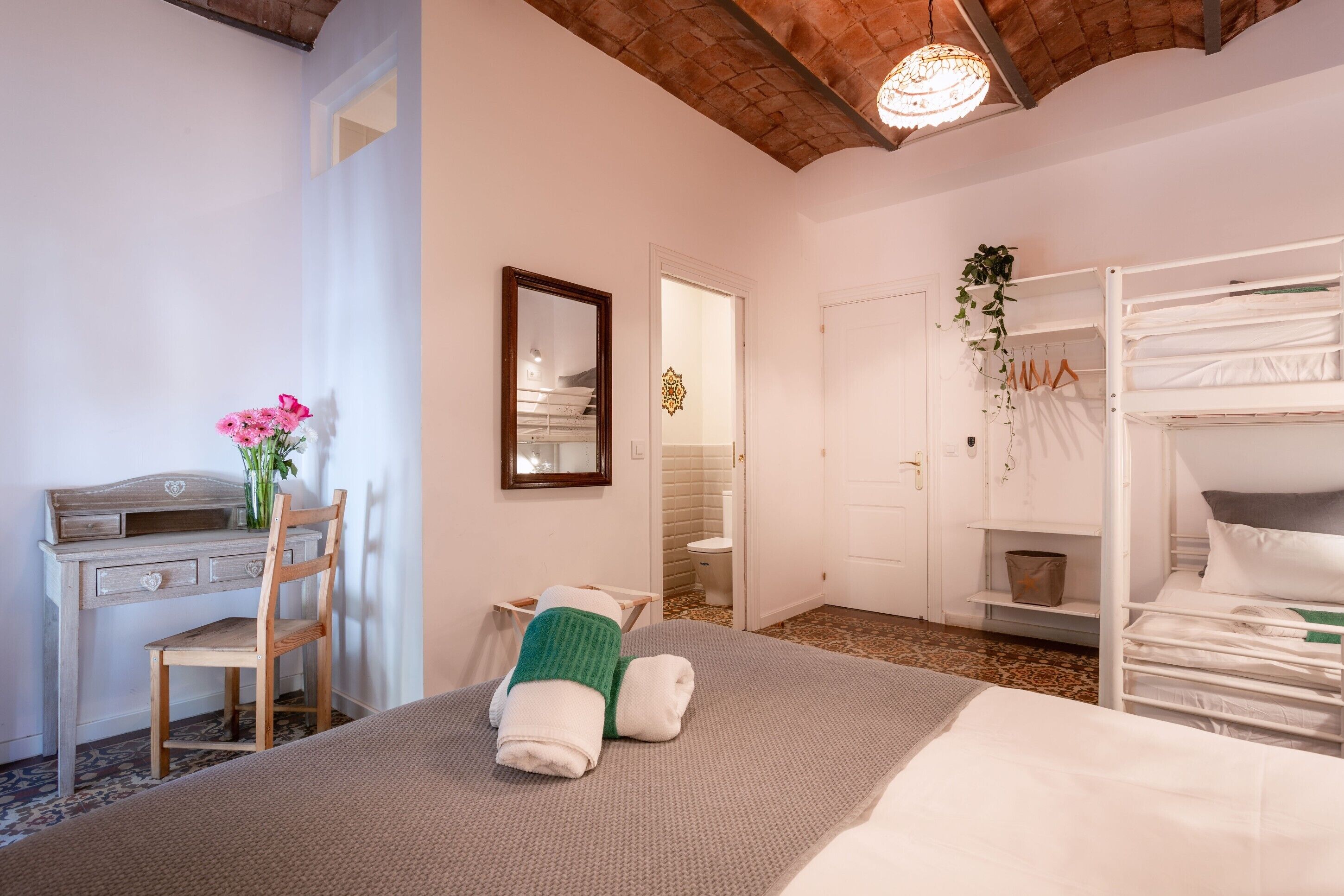 Un dormitorio con una cama litera, un escritorio con silla, un espejo y la puerta del baño.