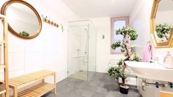 Un baño moderno con cabina de ducha de vidrio, un banco de madera, un lavabo con espejo y plantas en macetas.