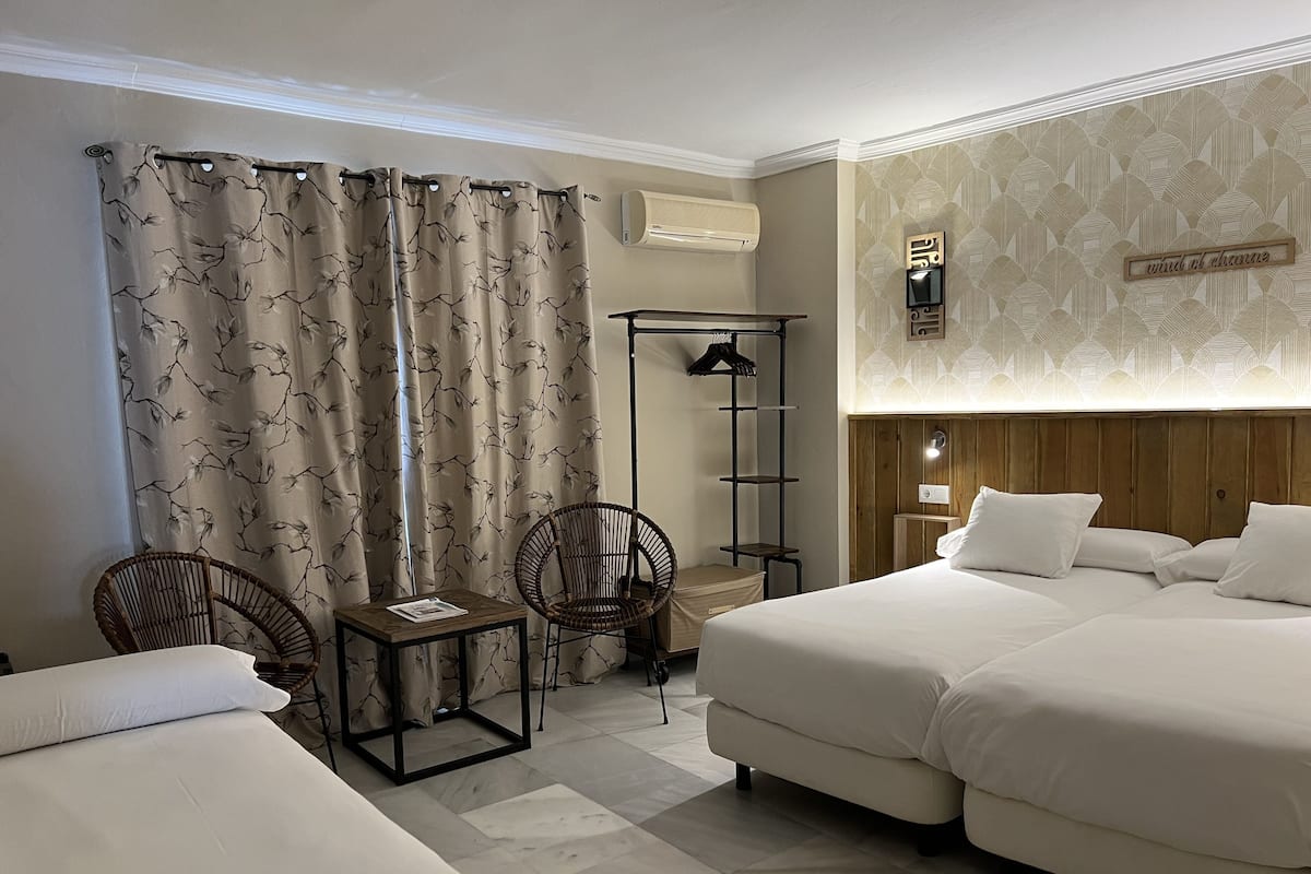 Habitació d'hotel amb dos llits, una taula petita, dues cadires, un armari i un aire condicionat fixat a la paret.